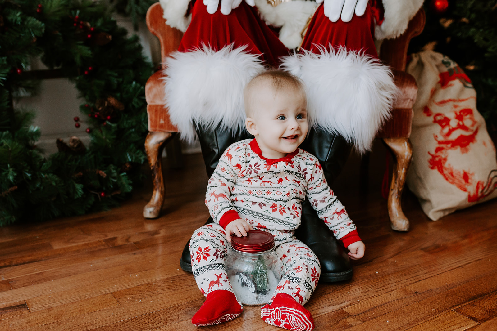 Baby sitting at Santa’s feet during a holiday mini session in Atlanta, GA. Captured by Santa session photographer Denay Shook, specializing in festive family photography.