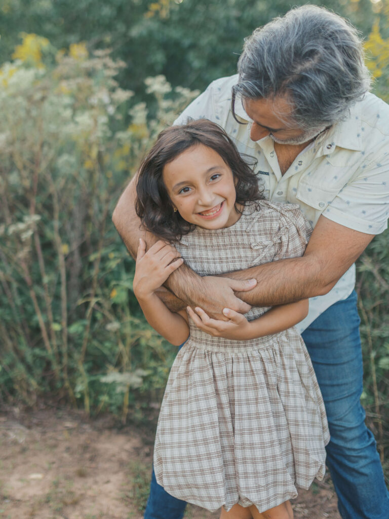 Father embracing his daughter while she laughs during a fall family photo session at Garrard Landing Park in Alpharetta, Georgia.