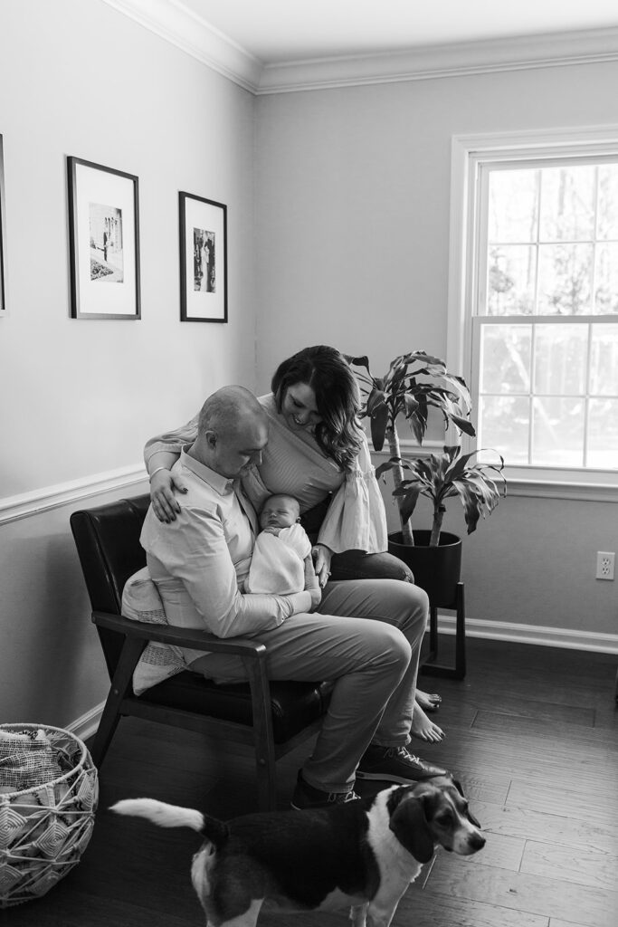 A family sits in their sitting room with their newborn baby and dog nearby