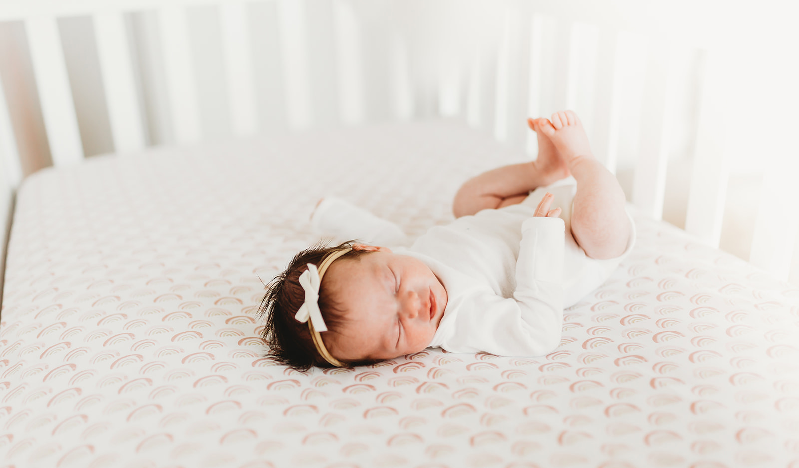 a newborn baby lays and stretches in their crib